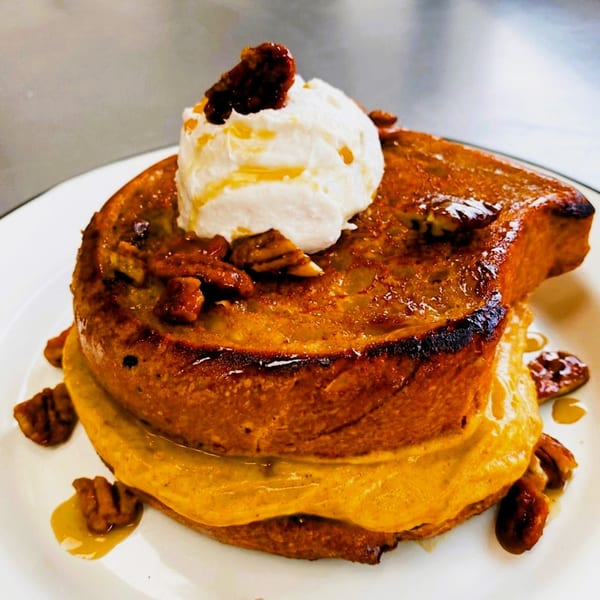 Vegan French toast stack with whipped cream, candied pecans, and syrup on a white plate.