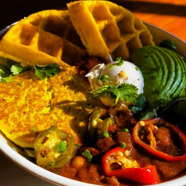 Vegan breakfast bowl with waffles, scrambled tofu, chili, avocado, and sour cream.