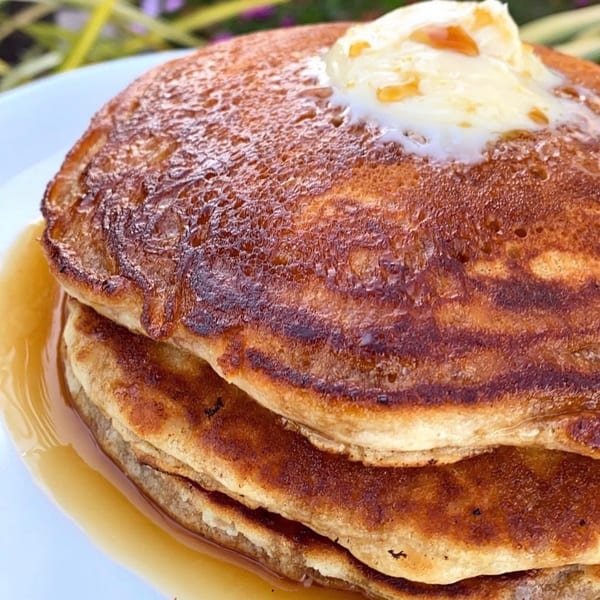Golden-brown pancakes topped with melting butter and syrup, served on a white plate.