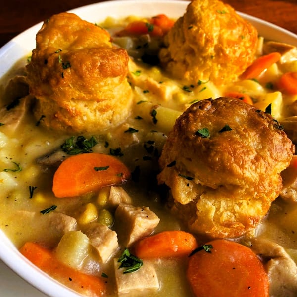 Close-up of vegan pot pie with golden biscuits, carrots, and plant-based protein in a creamy sauce.