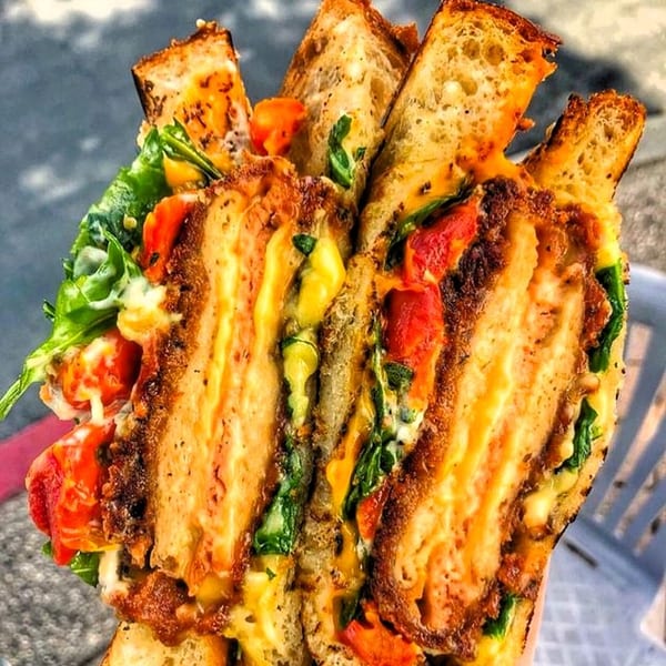 A close-up of a vegan grilled cheese sandwich with melted cheese, tomatoes, and greens.