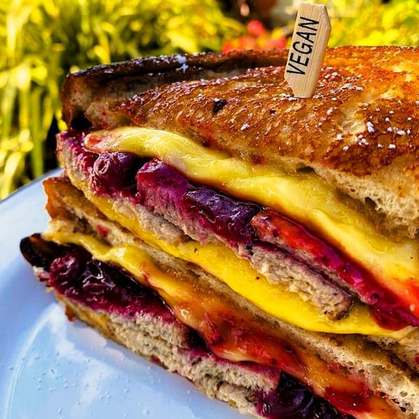 Close-up of a vegan grilled cheese sandwich with berry jam and a "VEGAN" pick.
