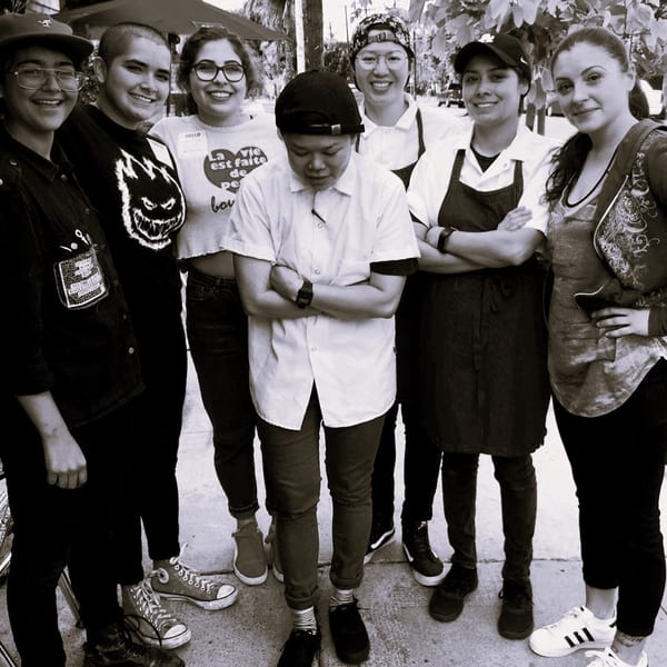 Seven smiling Wild Chive staff members, some in aprons, pose together outdoors.