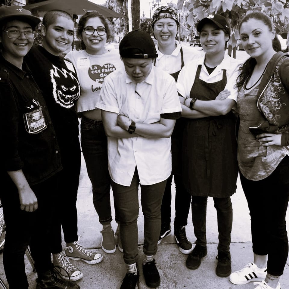 Seven smiling Wild Chive staff members, some in aprons, pose together outdoors.