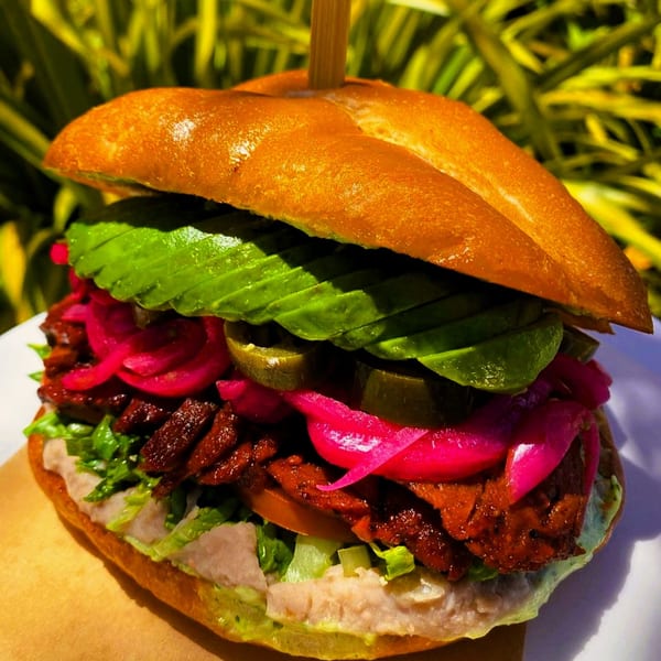 A vibrant vegan sandwich from The Wild Chive, featuring avocado, pickled onions, and jalapeños.